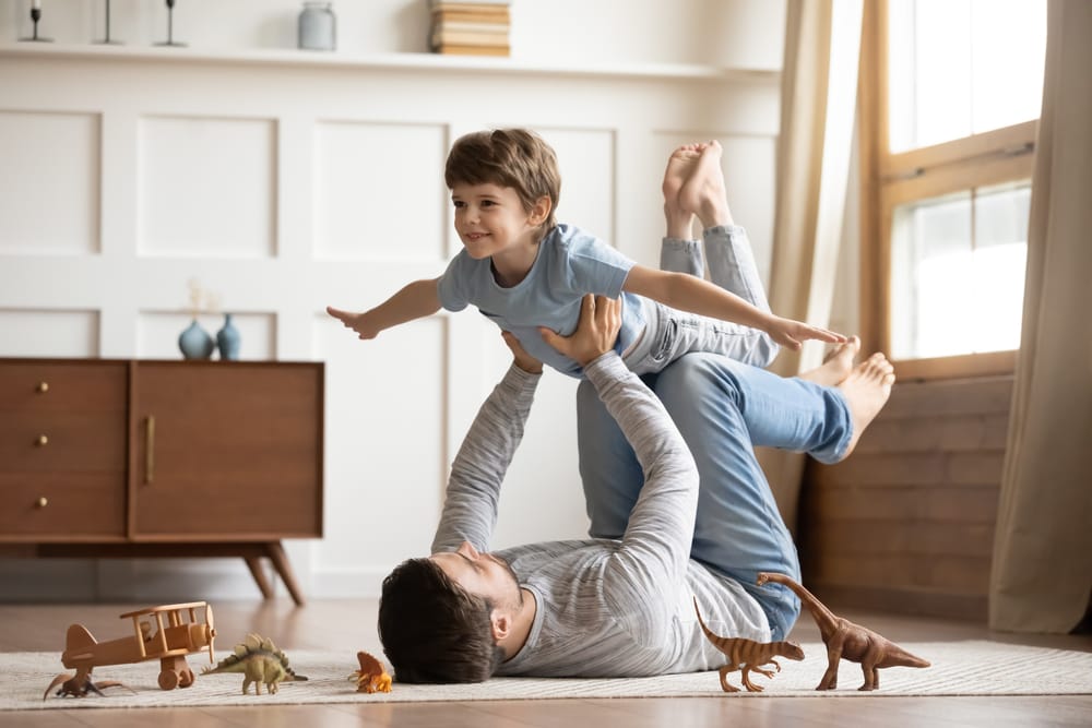 joyful,young,man,father,lying,on,carpet,floor,,lifting,excited