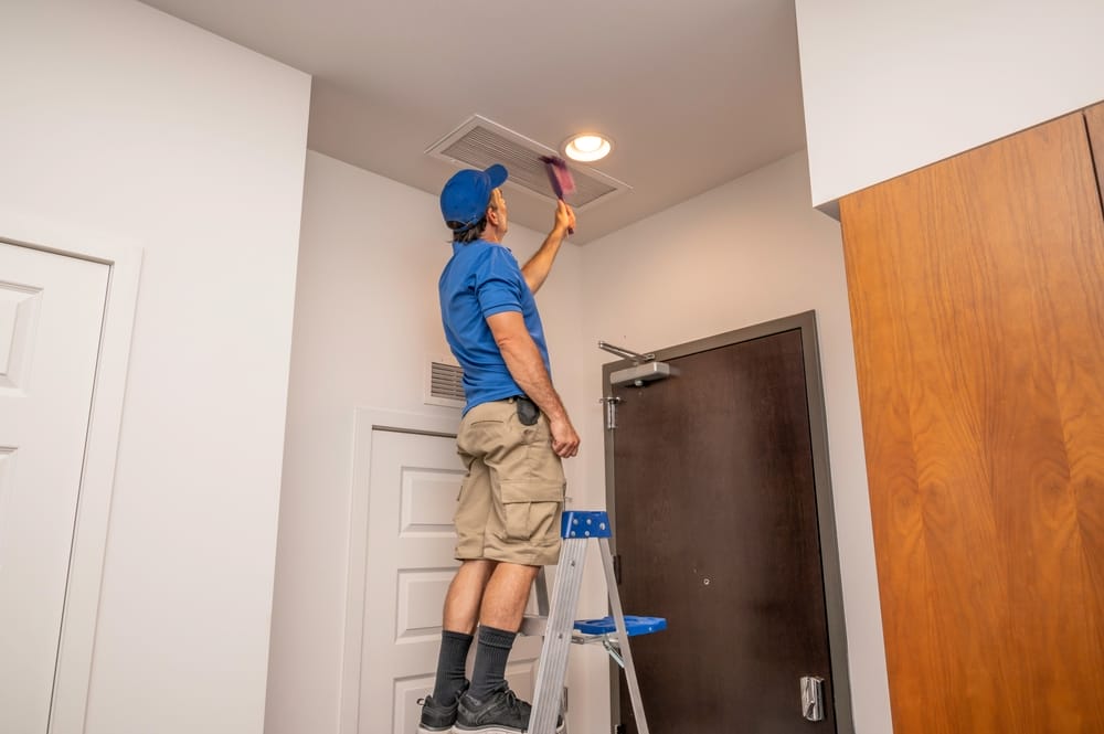 un homme à l'échelle nettoyant un conduit d'air de retour à l'intérieur