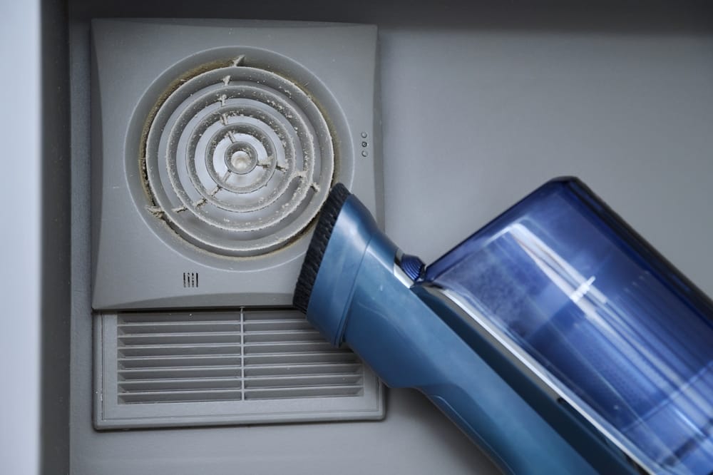 nettoyage de la grille de ventilation murale dans la salle de bain avec un aspirateur